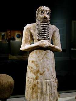 Ancient Sumerian bearded male statuette with folded hands and a long pleated garment
